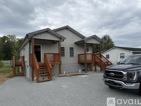 A grey house with a wooden deck and a Ford truck parked in front.