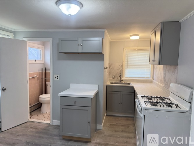A small, clean, and well-lit kitchen with a stove, sink, and cabinets.