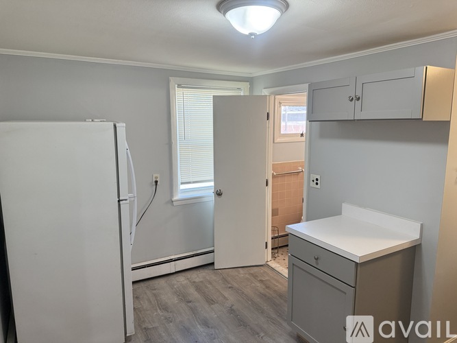 A kitchen area with a white fridge, a white counter, and a window with blinds.