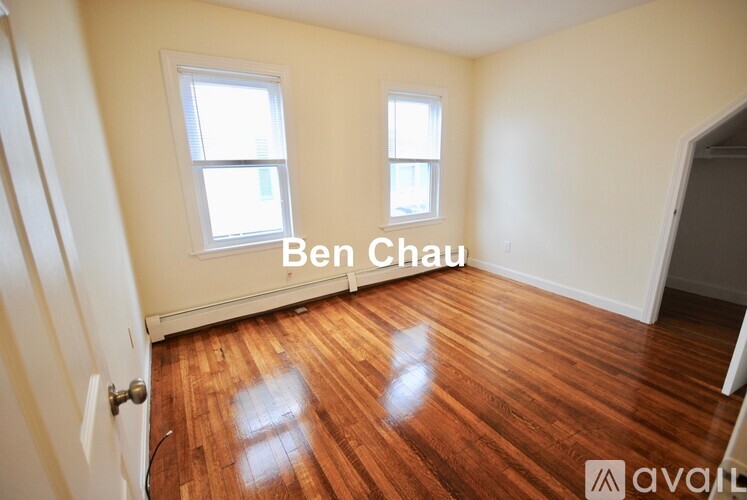 A room with wooden floors and two windows is available for rent.