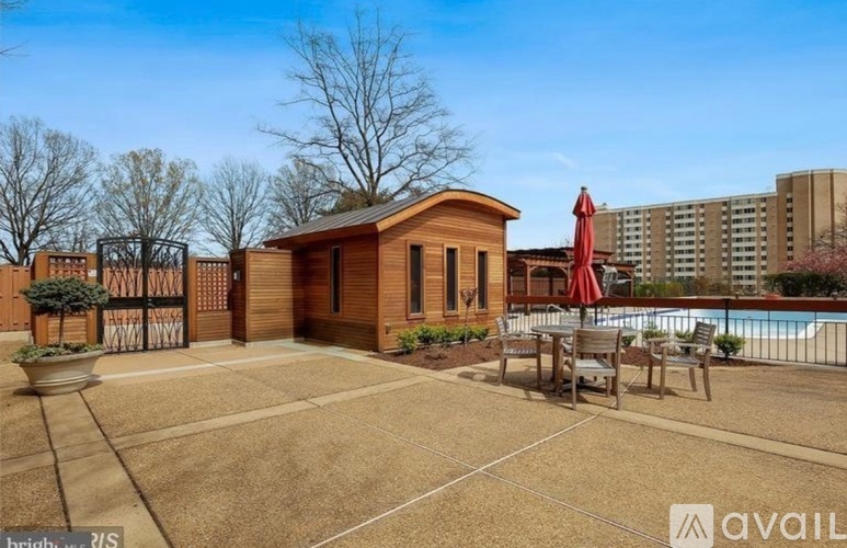 A small wooden cabin is surrounded by a pool and a fence.