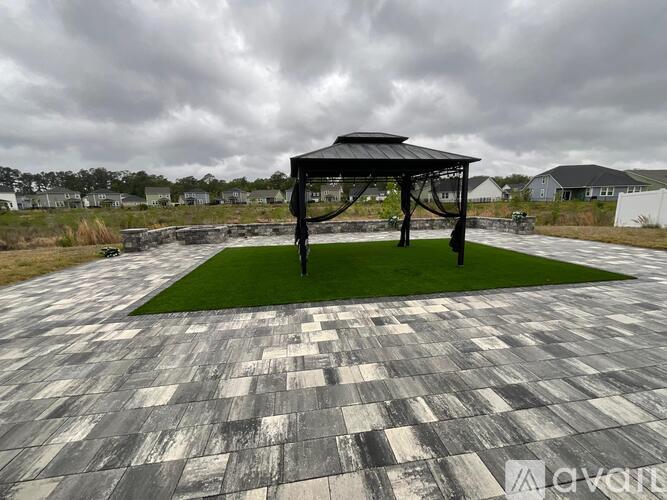 A pavilion with a black roof is situated on a grassy area with a checkered floor.