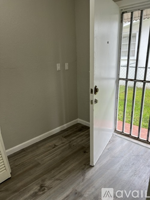 A room with a white door and a window with a view of a fence and grass.
