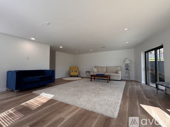 A spacious living room with a blue sofa, a white couch, and a rug on the wooden floor.