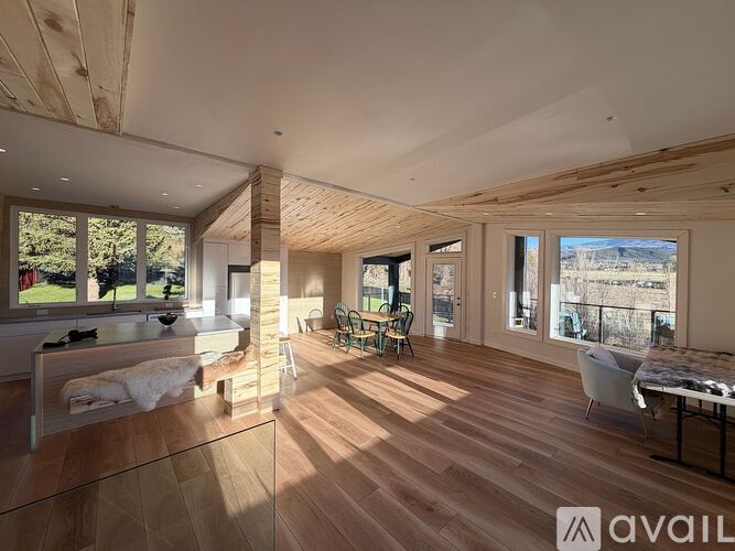A spacious room with wooden floors and a large window overlooking a grassy area.