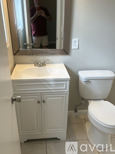 A man is taking a picture of a bathroom with a white toilet and sink.