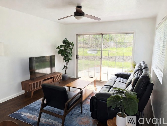 A living room with a black leather couch, a wooden coffee table, a flat screen TV, and a ceiling fan.