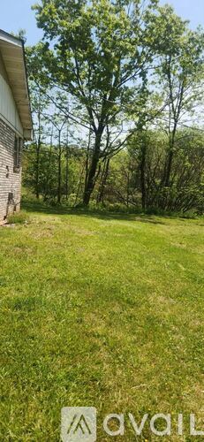 A grassy field with a house and trees in the background.