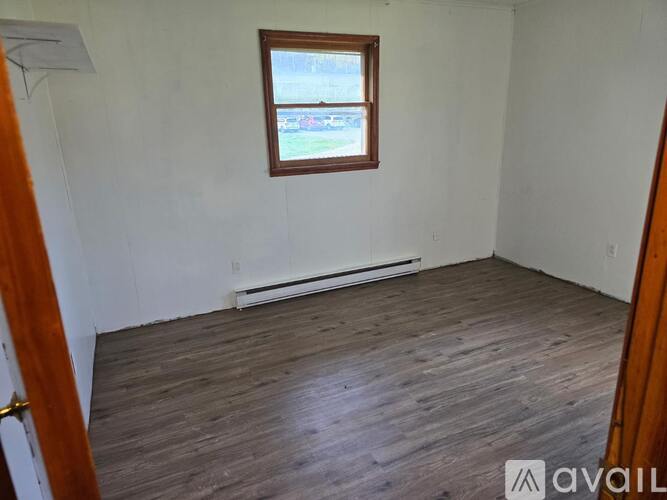 A room with wooden flooring and a window showing a parking lot outside.