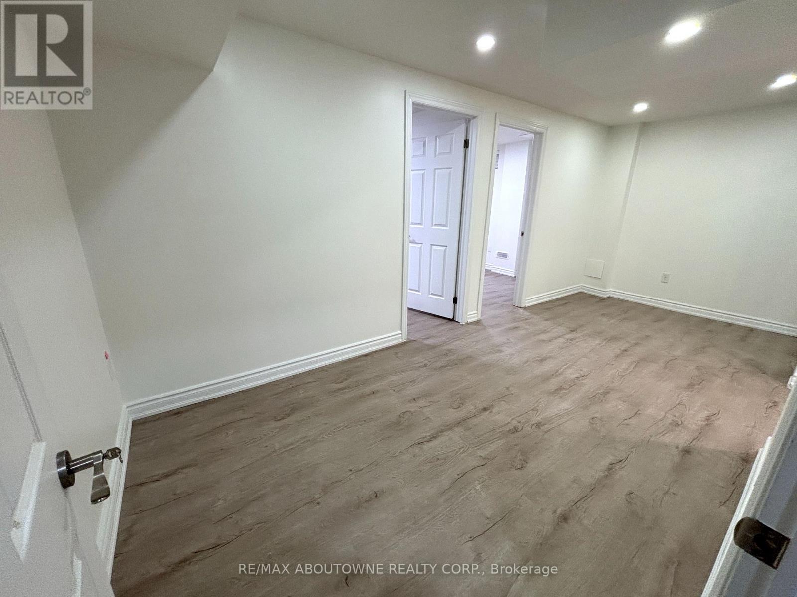 A room with a wooden floor and white walls, with a door in the background.