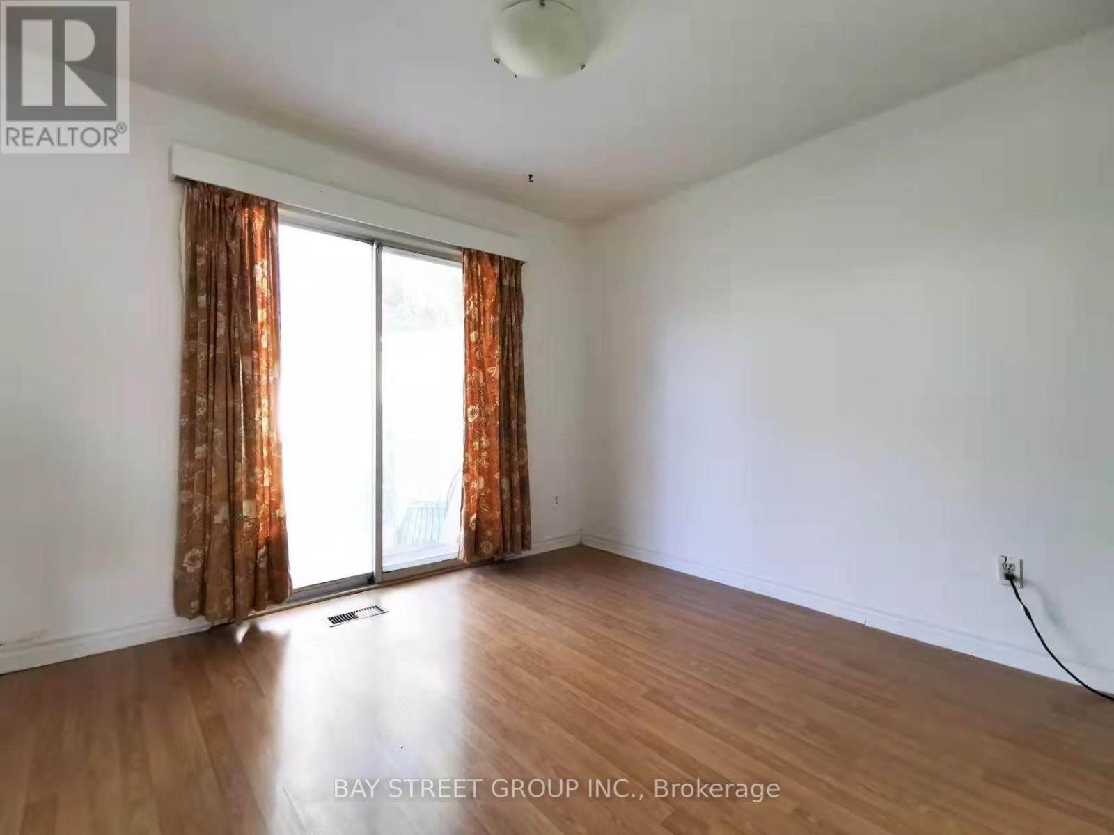 A room with a window and curtains, with a wooden floor and white walls.