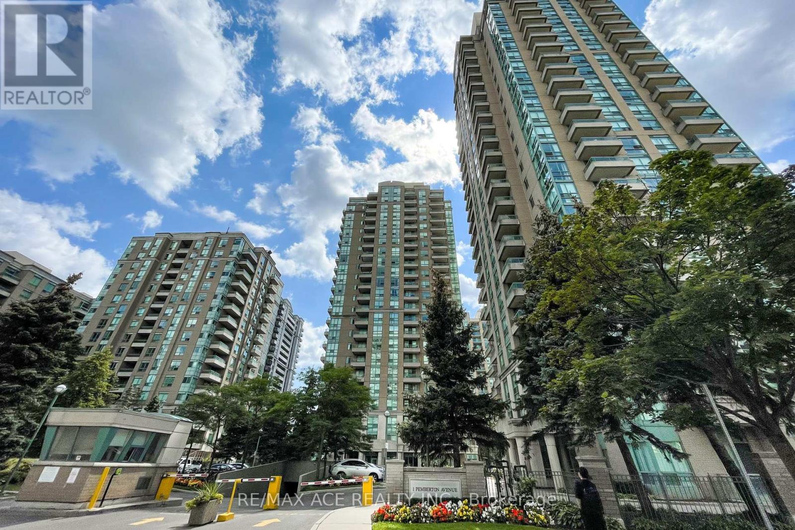 A tall building with a glass facade stands in front of a tree-lined street.