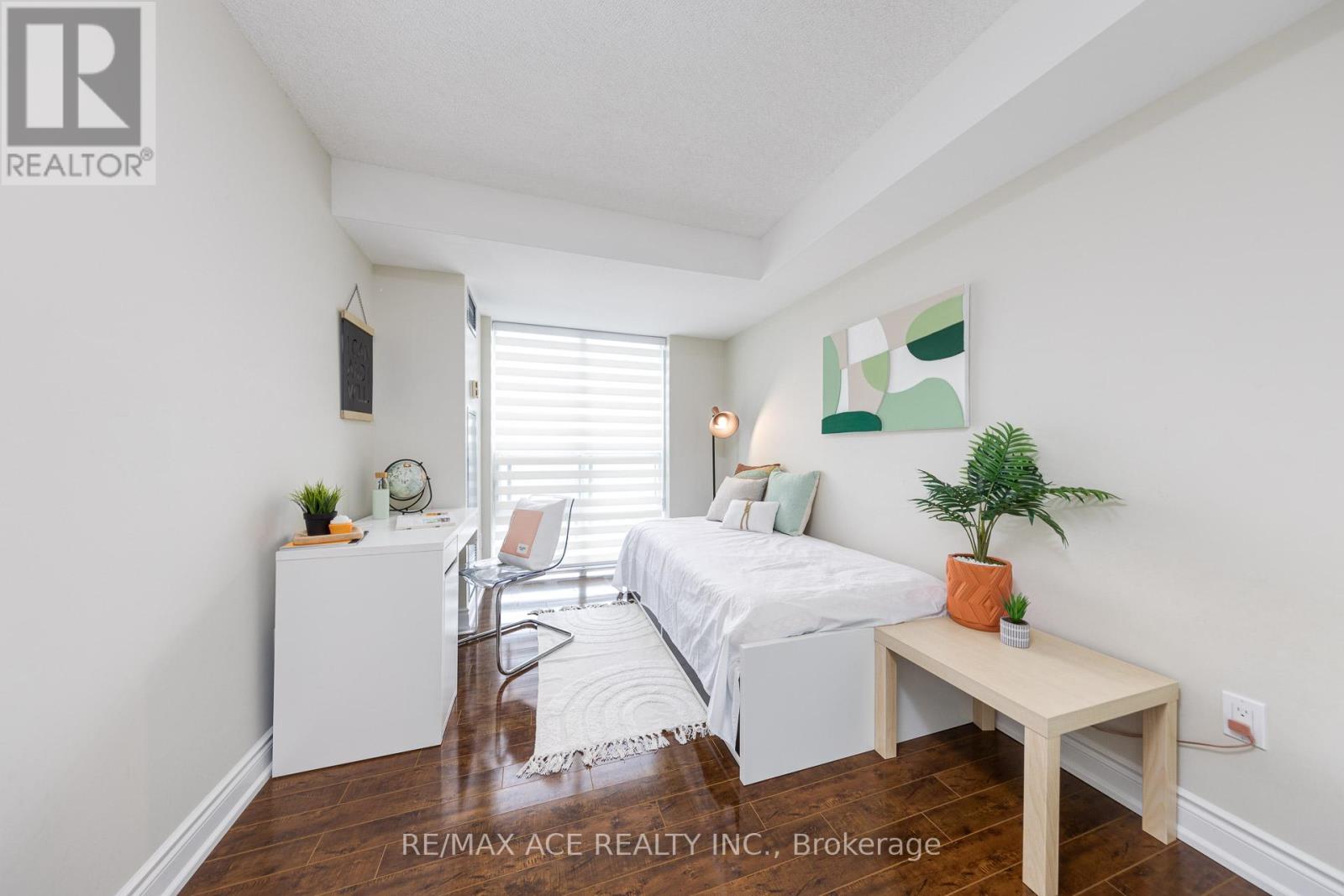 A bedroom with a bed, a chair, a table, and a plant.