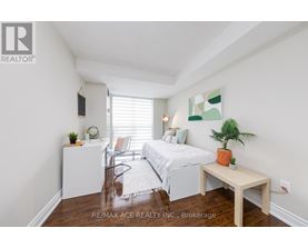 A bedroom with a bed, a chair, a table, and a plant.