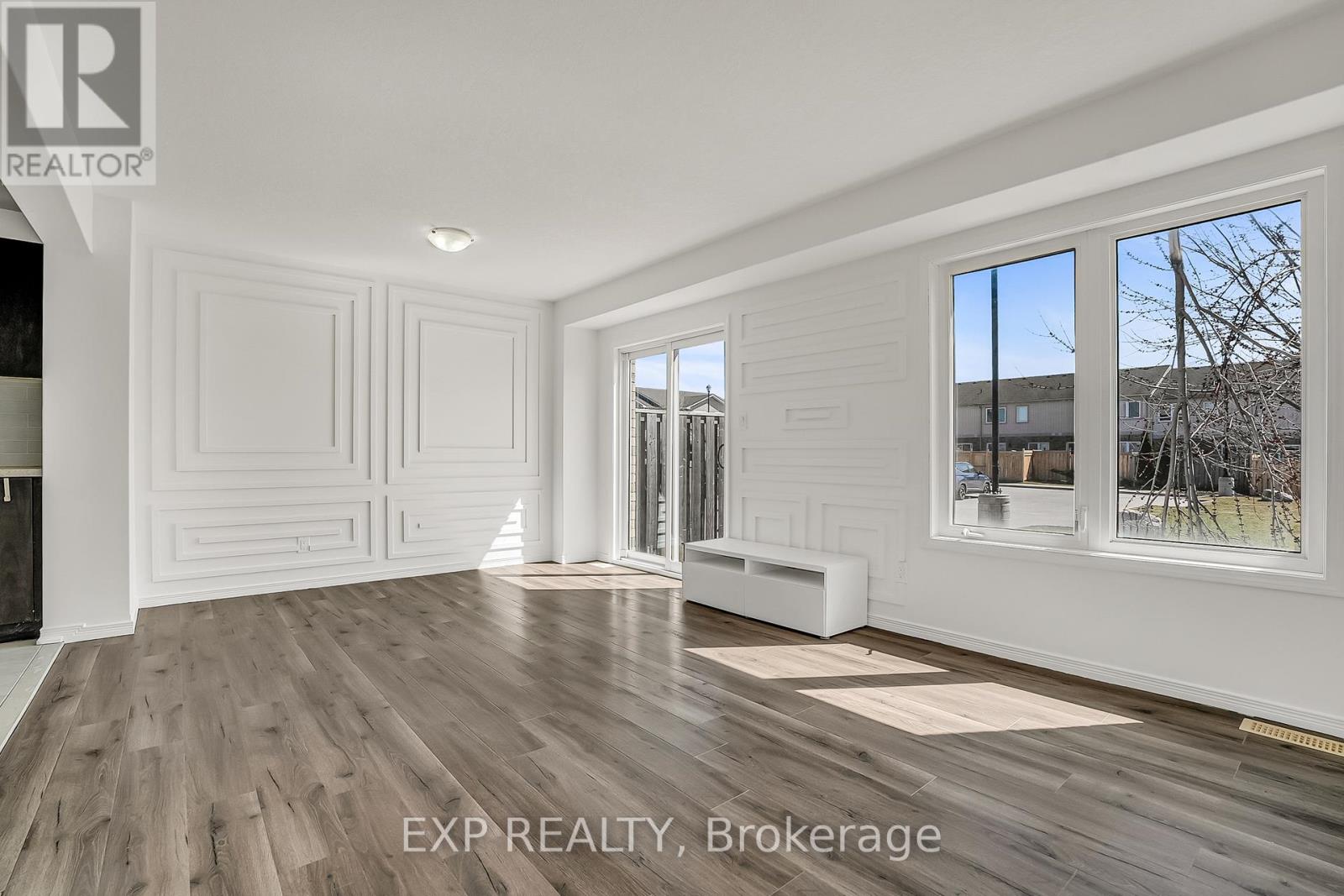 A room with white walls and wooden flooring, with a window showing a tree and a building outside.