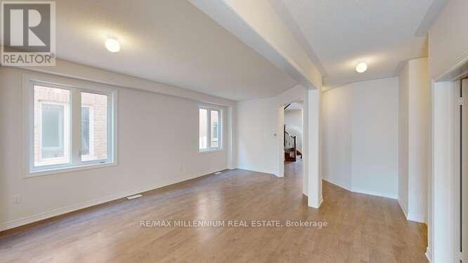 A spacious room with wooden floors and white walls, with a window on the left side.