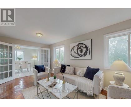 A living room with a white couch, a glass table, and a large abstract painting on the wall.
