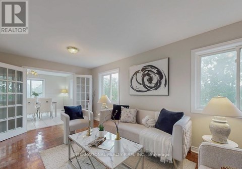 A living room with a white couch, a glass table, and a large abstract painting on the wall.