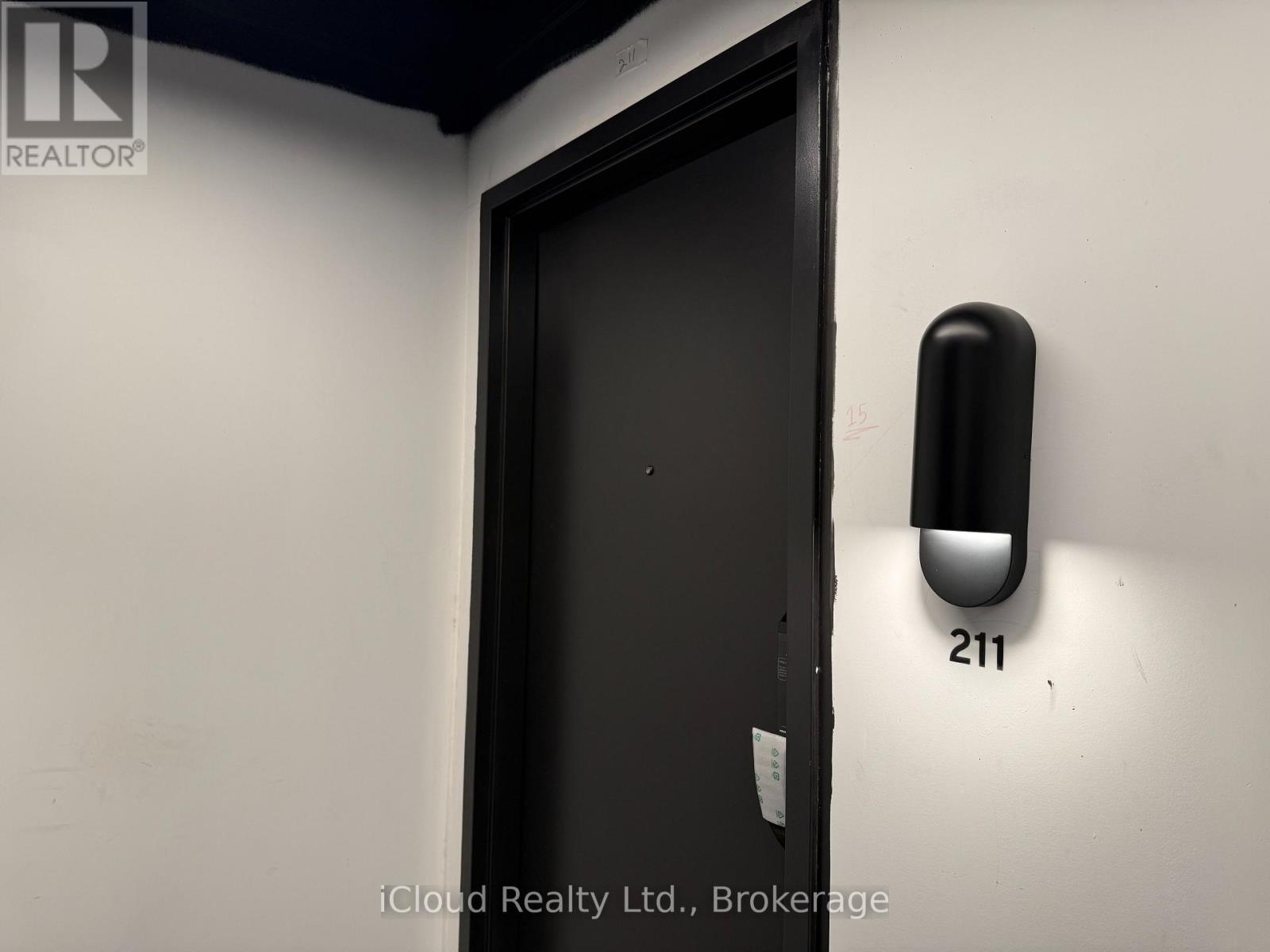A black door with a handle and a wall-mounted light fixture with the number 211 on it.