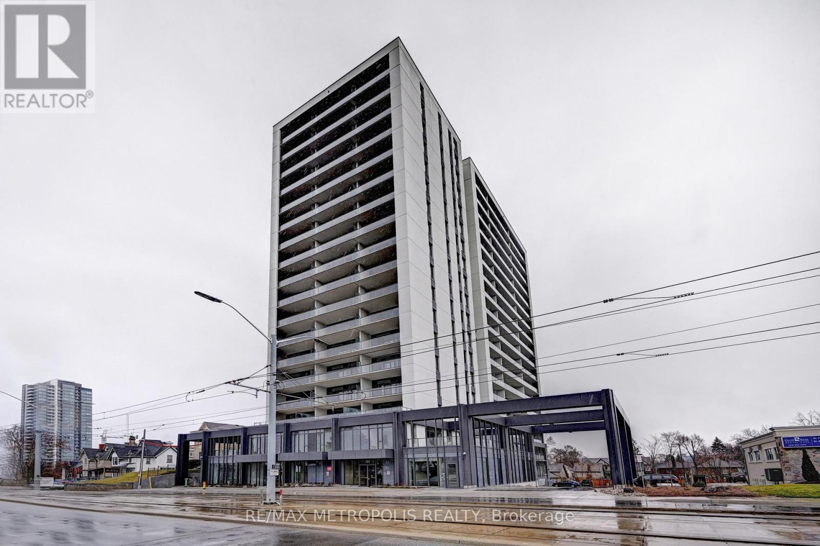 A tall building with a grey facade stands in the foreground of a city street.