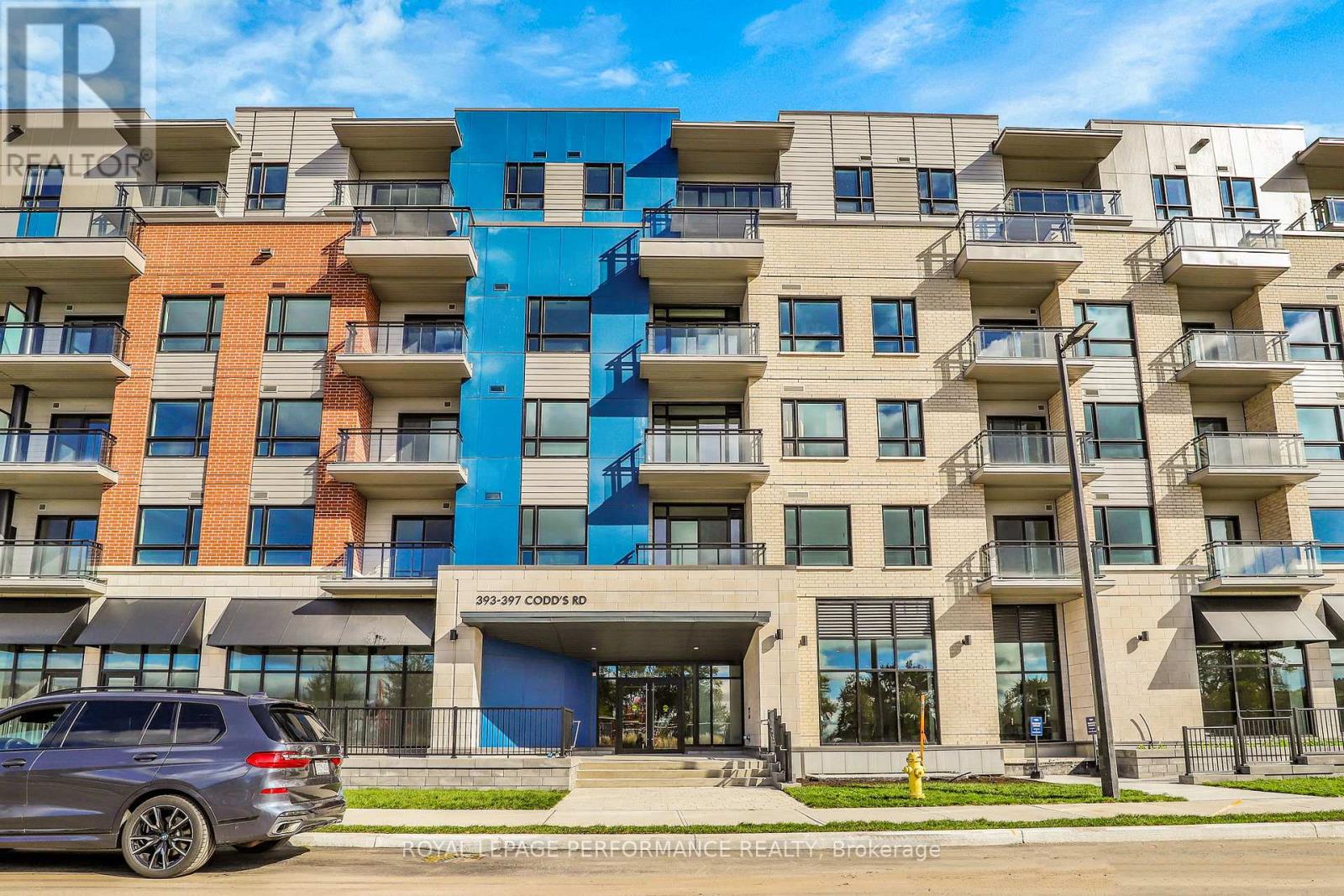 A modern apartment building with a blue car parked in front.