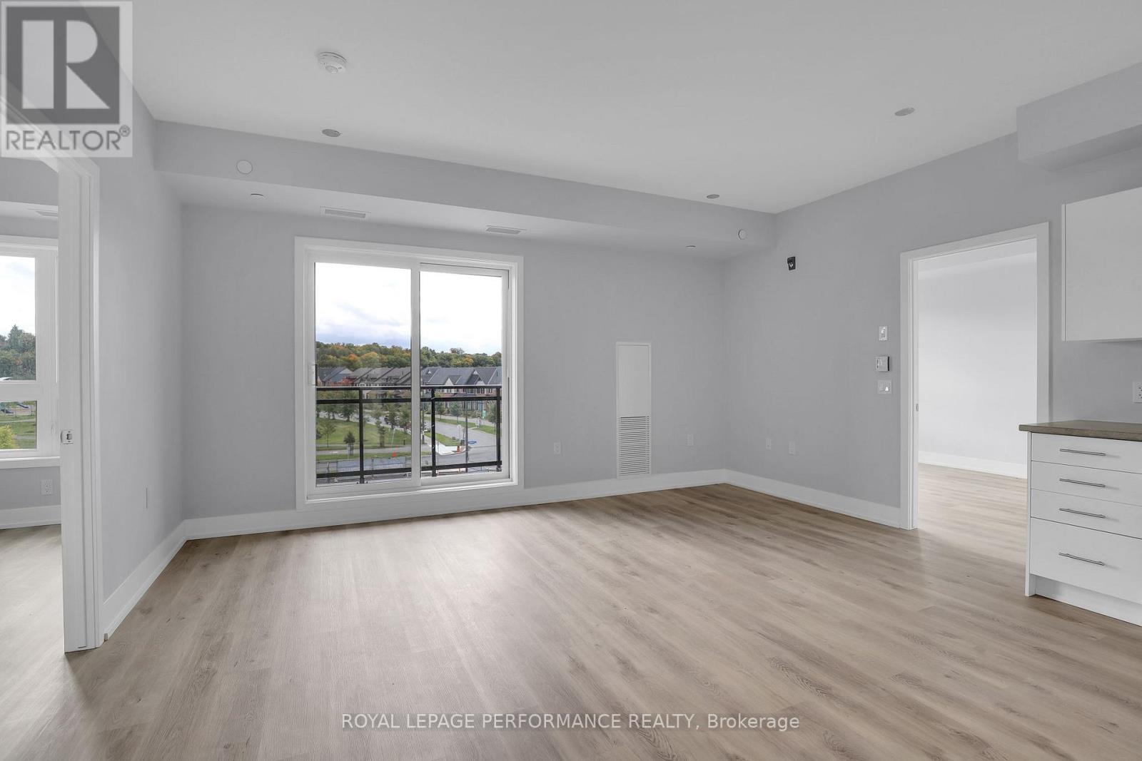 A spacious room with wooden flooring and a large window overlooking a street.