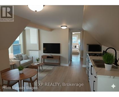 A living room with a television and a kitchen area in the background.