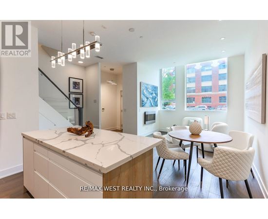 A modern kitchen with a marble island and white chairs.
