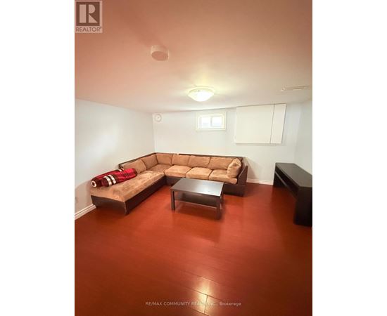 A brown couch with a red throw on it sits in a room with a wooden floor.