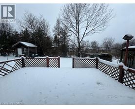 A snow-covered landscape with a wooden fence and a small building in the distance.
