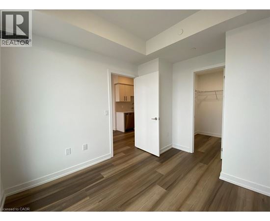 A room with white walls and wood flooring with a doorway leading to another room.