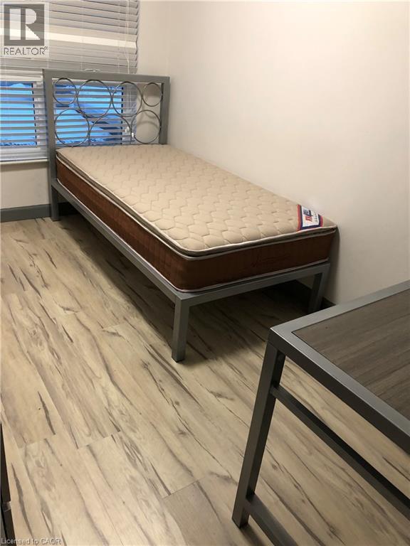 A mattress in a room with wooden flooring and a window with blinds.