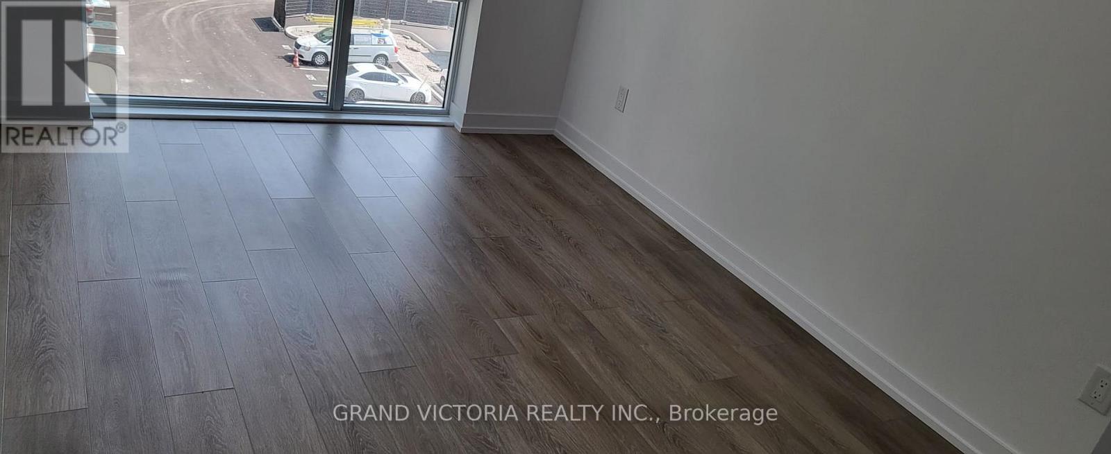 A room with a wooden floor and a large window overlooking a parking lot.