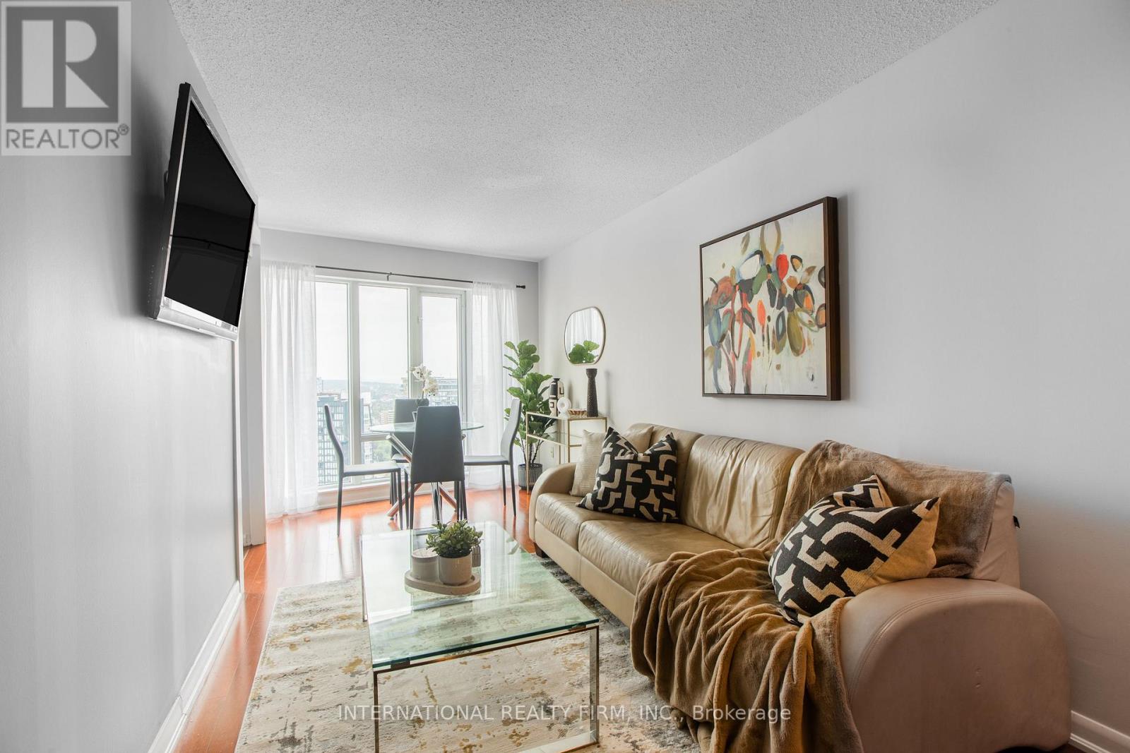A living room with a couch, a chair, a potted plant, and a television mounted on the wall.