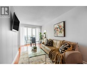 A living room with a couch, a chair, a potted plant, and a television mounted on the wall.
