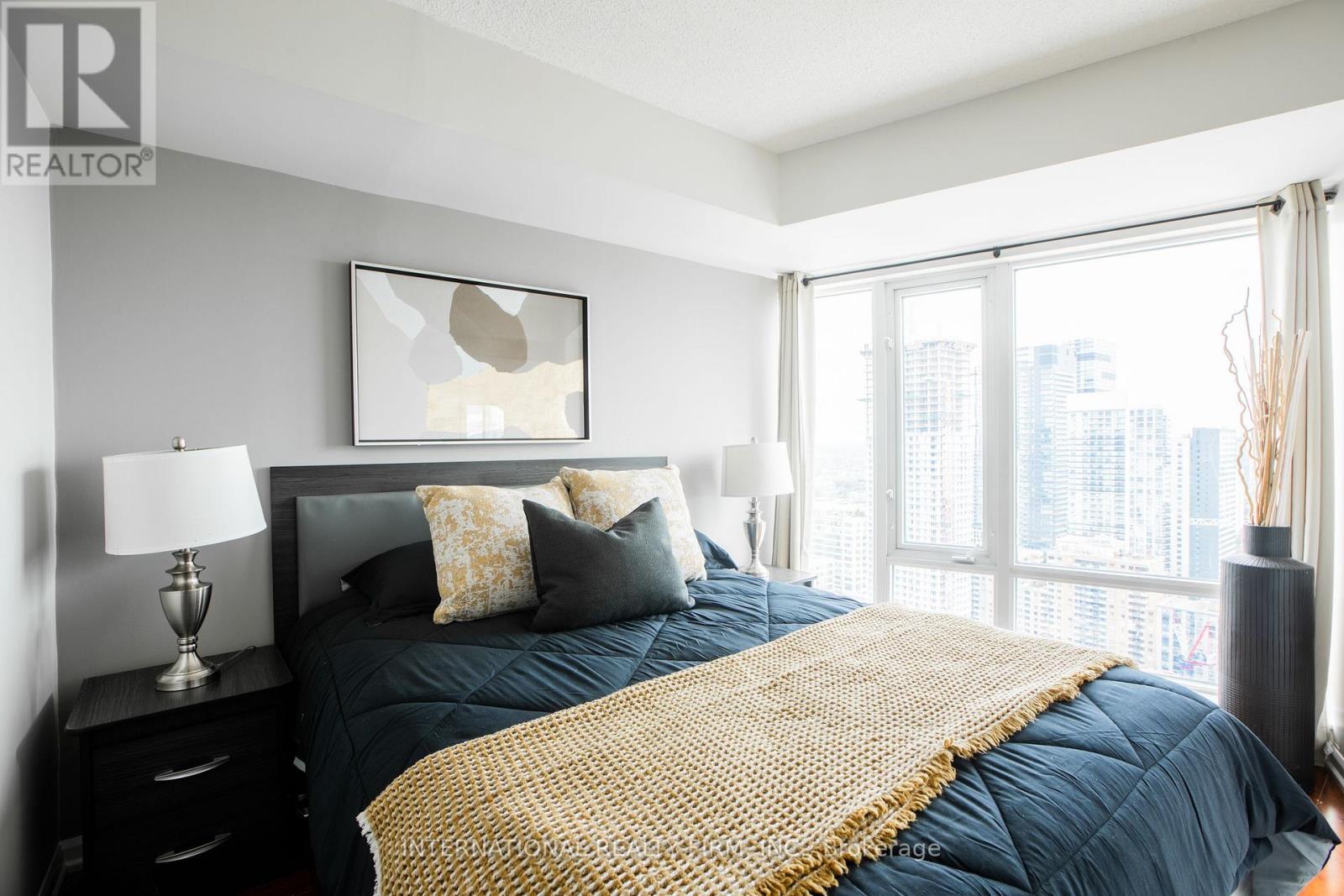 A bedroom with a large bed and a city view through the window.
