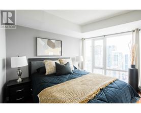 A bedroom with a large bed and a city view through the window.