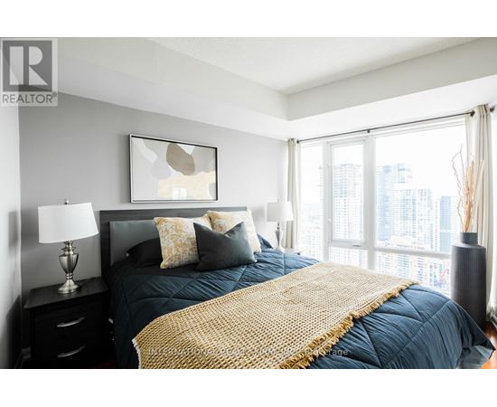 A bedroom with a large bed and a city view through the window.