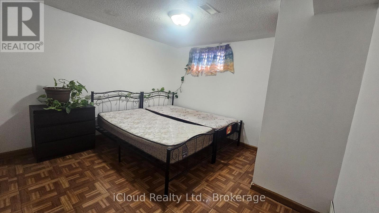 A bedroom with a bed, dresser, and plant.