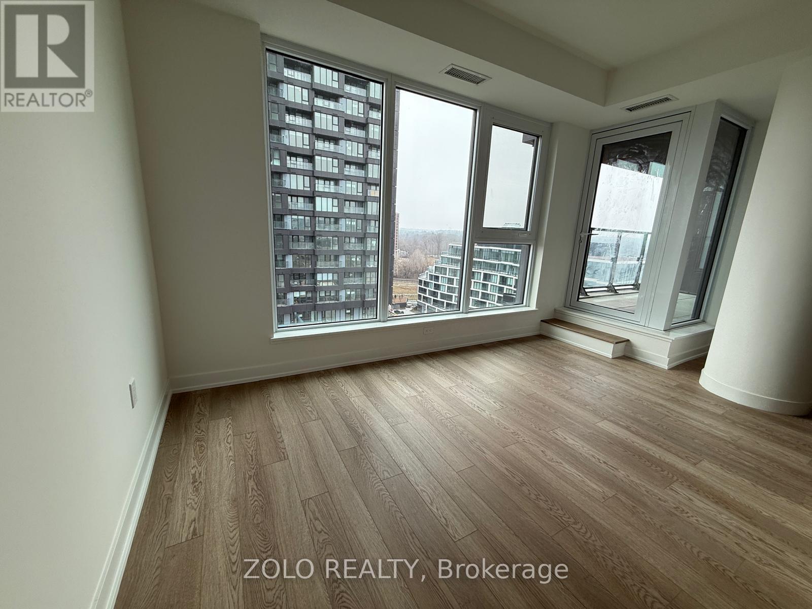 A room with wooden flooring and large windows overlooking a cityscape.