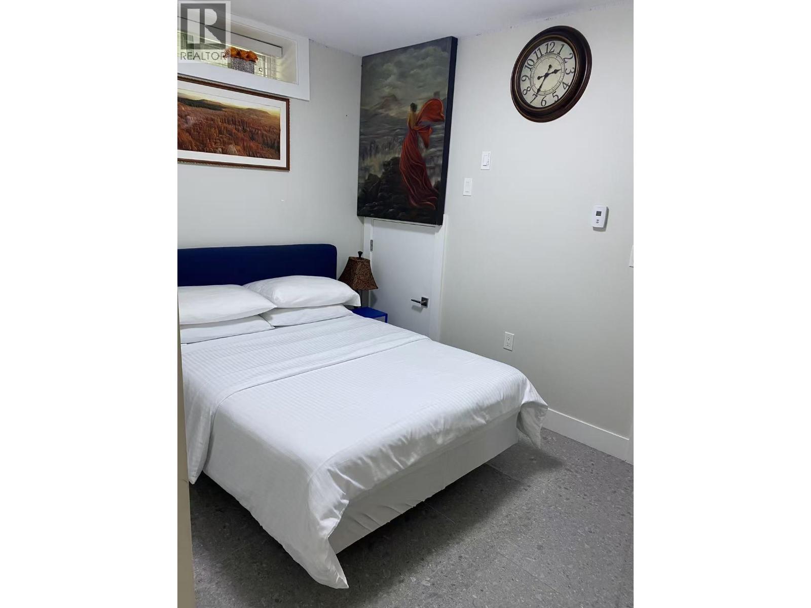 A bed with white sheets and a blue headboard is in a room with a clock on the wall.