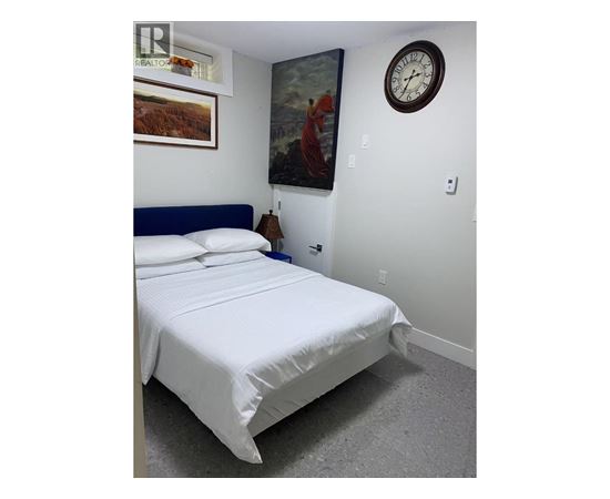 A bed with white sheets and a blue headboard is in a room with a clock on the wall.