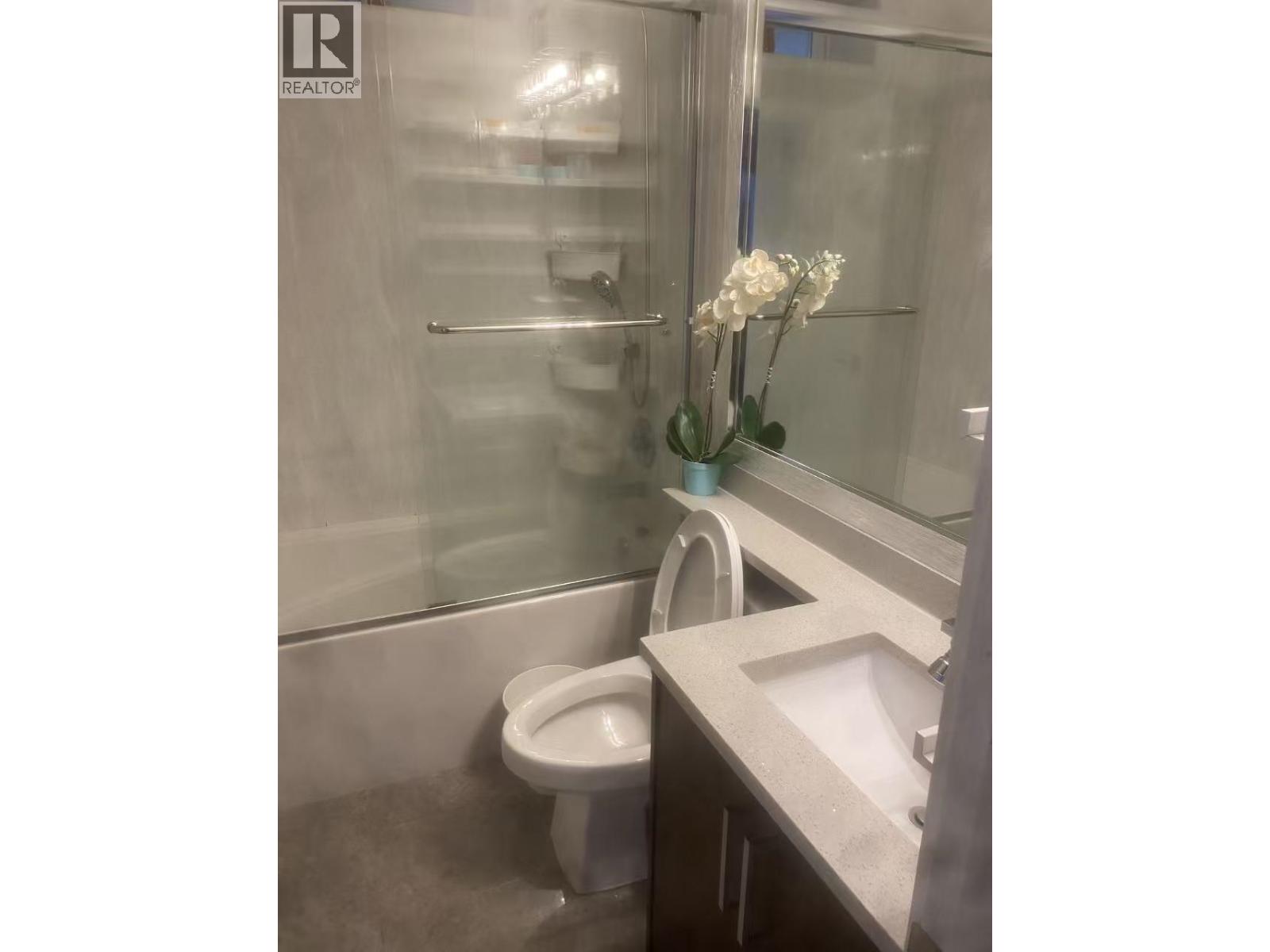 A white toilet is in a bathroom with a sink and a vase of flowers.