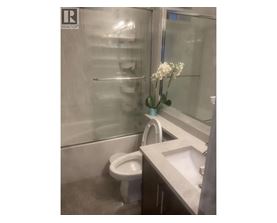 A white toilet is in a bathroom with a sink and a vase of flowers.