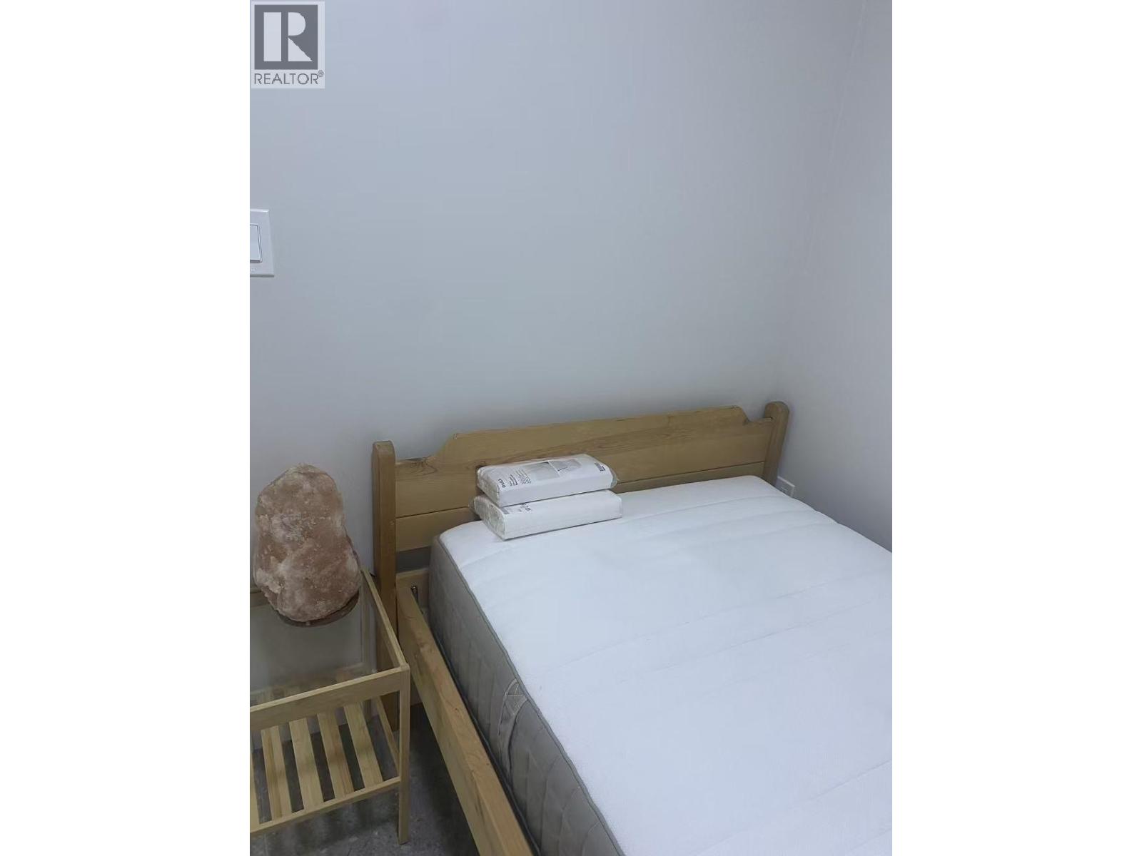 A bed with white sheets and a wooden headboard sits next to a nightstand with a rock on top.