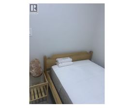 A bed with white sheets and a wooden headboard sits next to a nightstand with a rock on top.