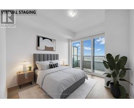 A bedroom with a large bed, a nightstand with a lamp, a potted plant, and a framed picture on the wall.