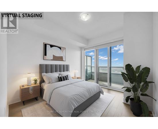 A bedroom with a large bed, a nightstand with a lamp, a potted plant, and a framed picture on the wall.