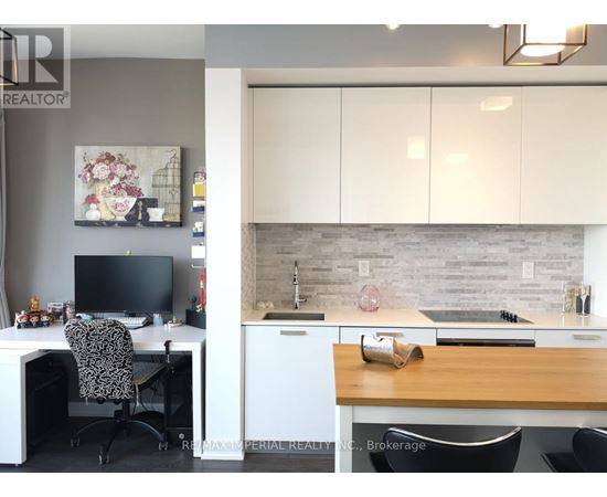A home office with a desk, chair, and a kitchen area with a sink and countertop.