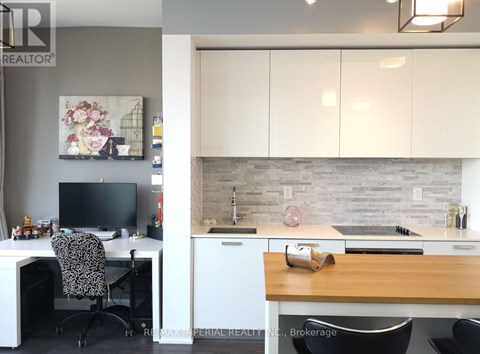 A home office with a desk, chair, and a kitchen area with a sink and countertop.